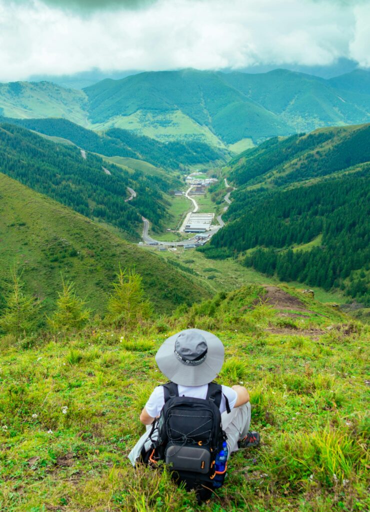 Backpacker resting on a lush green mountain overlooking a scenic valley.