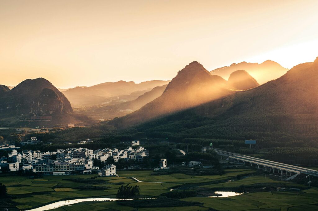 A serene sunset view of a countryside village nestled among scenic mountains.